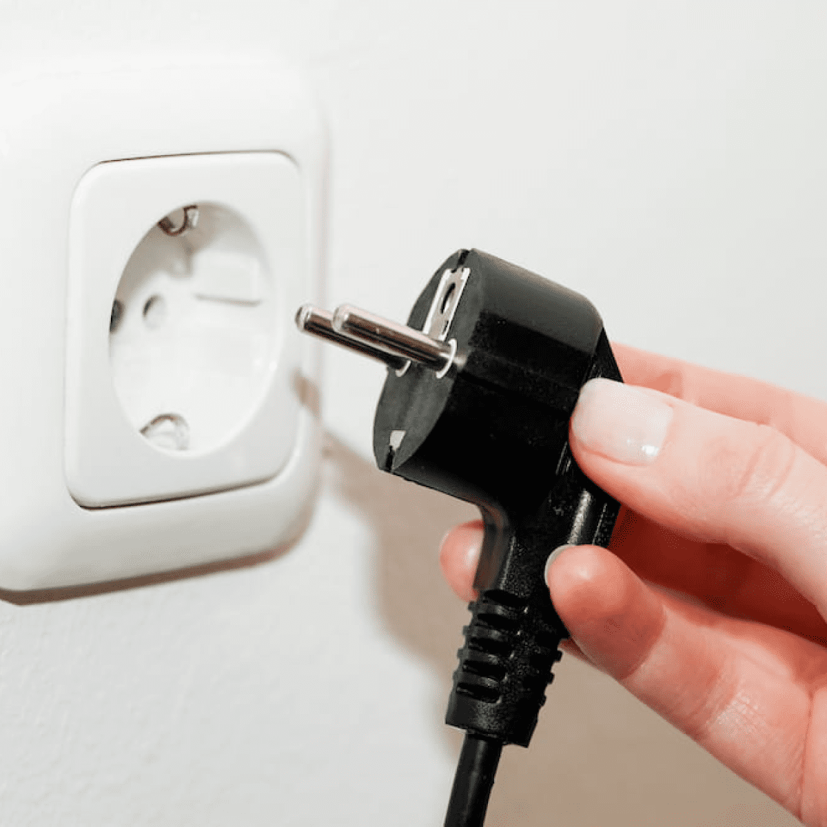 Person holding a schuko cable to plug it into the power socket